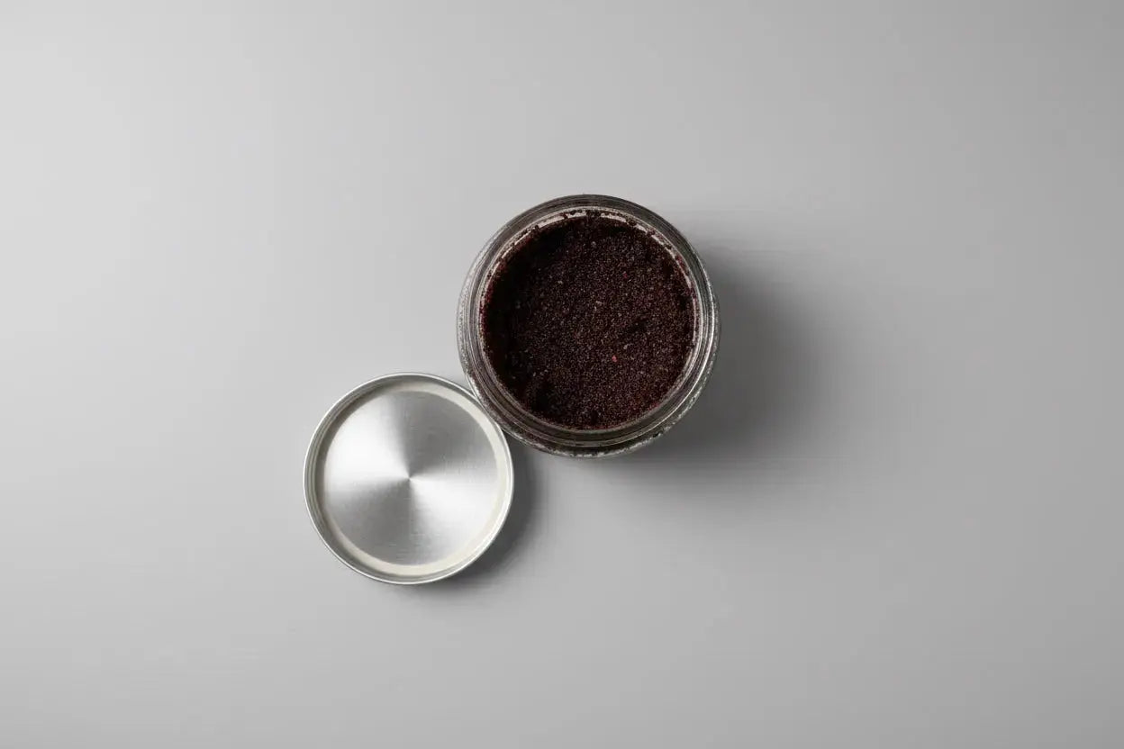 Jar of Xquisit Luxe coffee scrub with a metal lid on a gray surface